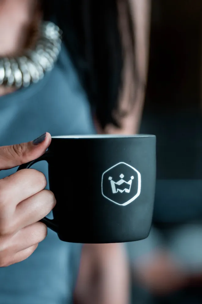 Software developer holding a black Ministry of Programming coffee mug, featuring the company logo, during a break in the office.