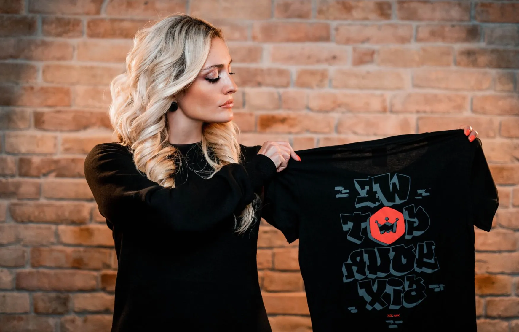 Ministry of Programming team member holding a MOP t-shirt in front of a brick wall